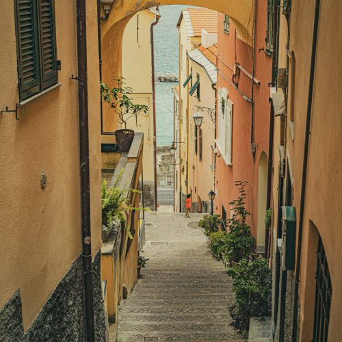 A picturesque view down a narrow alleyway leading to the sea in a historic coastal village.