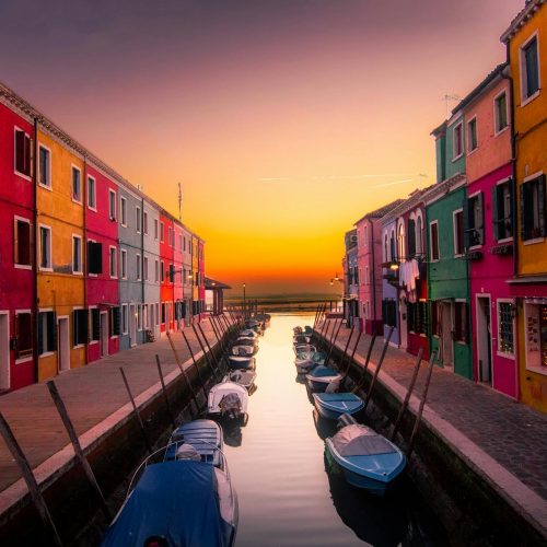 Vibrant facades along Burano's canal with boats at serene sunset. Perfect travel snapshot.
